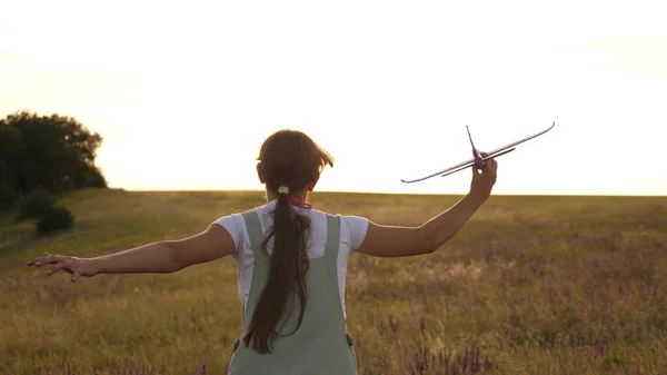 Ung flicka går med en leksak plan på fältet i strålarna av slint. barn leker leksaksflygplan. tonåring drömmer om att flyga och bli en pilot. flickan vill bli pilot och astronaut. — Stockfoto