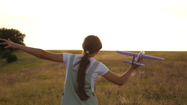 Ung flicka går med en leksak plan på fältet i strålarna av slint. barn leker leksaksflygplan. tonåring drömmer om att flyga och bli en pilot. flickan vill bli pilot och astronaut. — Stockfoto