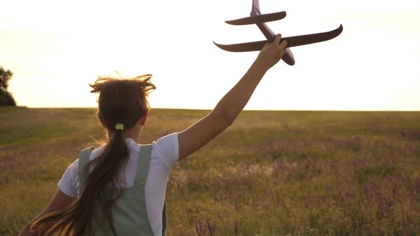 Ung flicka går med en leksak plan på fältet i strålarna av slint. barn leker leksaksflygplan. tonåring drömmer om att flyga och bli en pilot. flickan vill bli pilot och astronaut. — Stockfoto