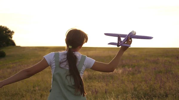 Giovane ragazza corre con un aereo giocattolo sul campo nei raggi di slint. i bambini giocano aereo giocattolo. adolescente sogna di volare e diventare un pilota. la ragazza vuole diventare un pilota e astronauta . — Foto Stock