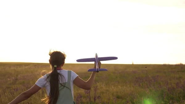 young girl runs with a toy plane on the field in the rays of slint. children play toy airplane. teenager dreams of flying and becoming a pilot. the girl wants to become a pilot and astronaut.
