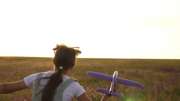Ung flicka går med en leksak plan på fältet i strålarna av slint. barn leker leksaksflygplan. tonåring drömmer om att flyga och bli en pilot. flickan vill bli pilot och astronaut. — Stockfoto