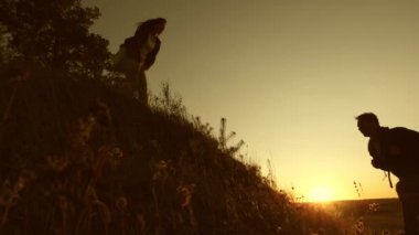 free Woman traveler holds out his hand to the traveler a man climbing to the top of the hill. teamwork tourists. adventure and travel concept. Tourists climb the mountain at sunset, holding hands.