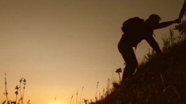 free Woman traveler holds out his hand to the traveler a man climbing to the top of the hill. teamwork tourists. adventure and travel concept. Tourists climb the mountain at sunset, holding hands.