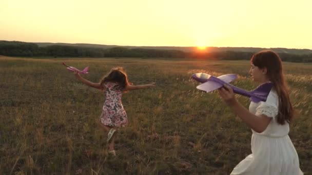 Мечтает летать. Счастливое детство. Две девушки играют с игрушечным самолетом на закате. Дети на фоне солнца с самолетом в руке. Силуэт детей, играющих в самолете — стоковое видео