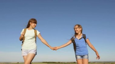 girls tourists go holding hands. free girl travelers travel with backpacks in the countryside. teamwork tourists teenagers. Happy girls travelers go with backpacks in field.