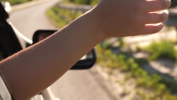 Vrouwelijke reiziger rijdt met de auto. een hand van het autoraam vangt de wind op. Meisje met lang haar zit voorin in de auto, strekt haar arm uit het raam en vangt verblindende zon — Stockvideo