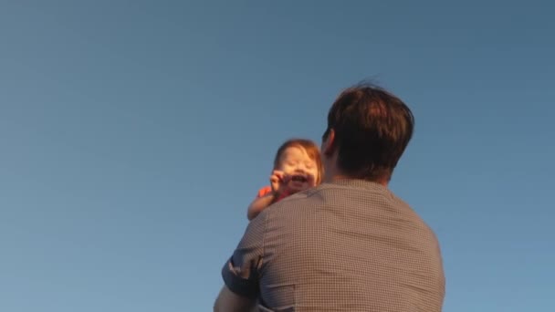 Conceito de infância feliz. pai joga seu filho no céu azul papai brinca com uma filhinha, o bebê sorri e se alegra. Movimento lento. família feliz jogando à noite contra o céu . — Vídeo de Stock