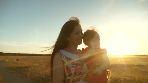 Mom and little daughter are walking along a country road in a wheat field. mother and baby walks in nature. Happy mom walks with the baby in her arms. Daughter holds mom by the chest. — Stock Video