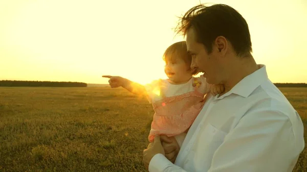 Father teaches little daughter in the park. concept of a happy family and childhood. Dad and mom playing with a little daughter in her arms at sunset. family walks with the child at sunset. — Stockfoto