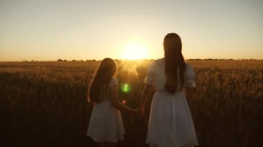 Anne, güzel bir gün batımının arka planında kızına nazikçe sarılıyor. Yetişkin bir kız, annesinin kollarında güneşin altında bir tarlada. Anne kızının saçlarını okşar..