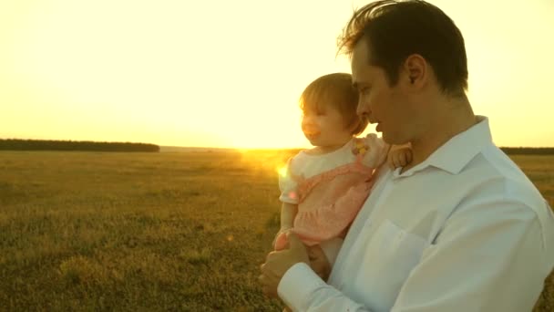 Father teaches little daughter in the park. concept of a happy family and childhood. Dad and mom playing with a little daughter in her arms at sunset. family walks with the child at sunset. — ストック動画