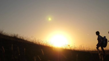 sırt çantaları ile çocuklar ve anne güneşte dağa tırmanmak seyahat. Anne ve kızları kampa gidiyor. Gün batımında seyahat eden çocukları olan turist ailesi. turistlerin ortak çalışma. zafere hareket.