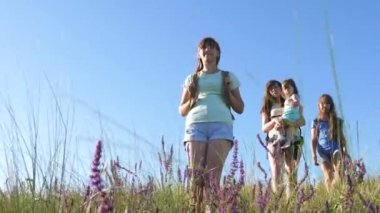 Özgür kadın gezginler dağdan çiçek tarlası boyunca inerler. Yürüyüşçü kız. Kadın turistler gün batımında seyahat eder. Sırt çantalı anne ve kızları güneşin altında yokuş aşağı gidiyorlar. turist takım çalışması