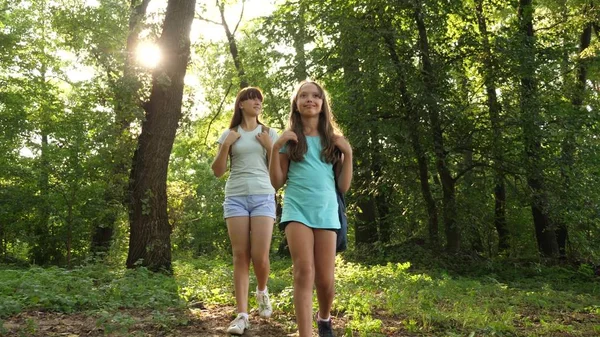 Mädchen mit Rucksäcken gehen durch das Dickicht im Wald. Kindertouristen sind im Sommerpark unterwegs. Teenager auf der Suche nach Abenteuer. Wanderin. Teamwork-Touristen — Stockfoto