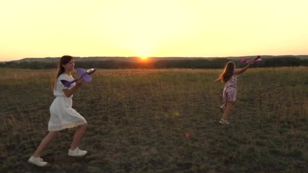 Sueños de volar. Concepto de infancia feliz. Dos chicas juegan con un avión de juguete al atardecer. Niños en el fondo del sol con un avión en la mano. Silueta de niños jugando en el avión — Vídeos de Stock