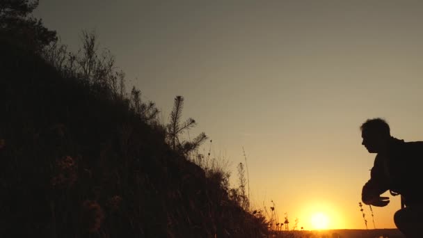 Vrije reizigers beklimmen een berg bij zonsondergang hand in hand. mannelijke toerist houdt de hand van een vrouwelijke reiziger, klimmen naar de top van de heuvel. teamwork van zakenmensen. — Stockvideo