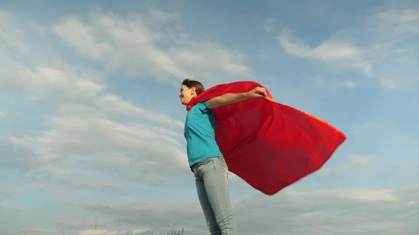 Kind speelt in rode jas, droom ervan om een held Supervrouw te worden. prachtig meisje superheld staat op het veld in een rode mantel, mantel fladderen in de wind. Langzame beweging. meisje droomt ervan om een superheld te worden. — Stockfoto