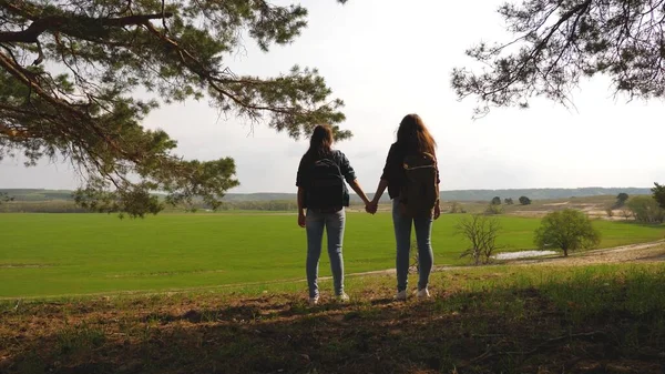 Gratis kvinnor turister på semester resa genom skogen med en ryggsäck, upp med händerna. Vandrarflickor lagarbete. Resenärsflickor sträcker upp sina händer, firar seger och njuter av landskapet. — Stockfoto