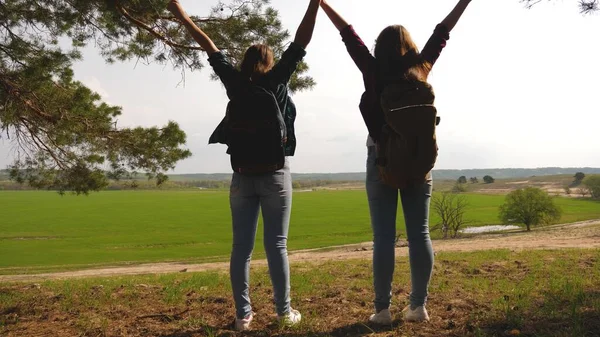 Freie Touristinnen im Urlaub reisen mit einem Rucksack durch die Wälder, heben die Hände. Teamwork bei den Wandermädchen. Wandermädchen heben die Hände, feiern den Sieg und genießen die Landschaft. — Stockfoto