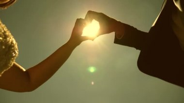 elinde güneş. Ufukta güneşin karşısında elleri ile bir kalp sembolü yapan sevgi dolu bir çift siluet. sevgi dolu çiftin takım çalışması. Düğün günü kutlaması