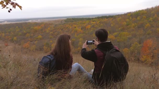 Wolny mężczyzna i kobieta z plecakami robią sobie selfie na górze. podróżni są fotografowane przez telefon przed pięknym krajobrazem. turyści robią zdjęcia dla pamięci. podróżnych do pracy zespołowej. koncepcja przygody — Wideo stockowe