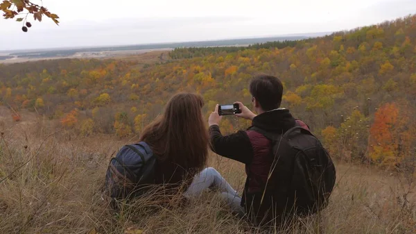 Volný muž a žena s batohy vzít selfie na horu. cestovatelé jsou fotografováni na telefonu proti krásné krajině. turisté fotit pro paměť. Týmová práce poutníků. koncept dobrodružství — Stock fotografie