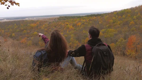 Reizigers in de herfst zitten op een heuvel en genieten van het herfstlandschap. teamwerk. Het concept van sportief toerisme. toeristen rusten en kijken uit over de verte vanaf de top van de berg. — Stockfoto
