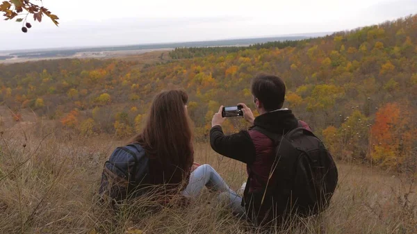 Fri man och kvinna med ryggsäckar ta selfies på berget. Resenärer fotograferas på telefon mot vackert landskap. turister ta bilder för minne. Lagarbete resenärer. äventyrskoncept — Stockfoto
