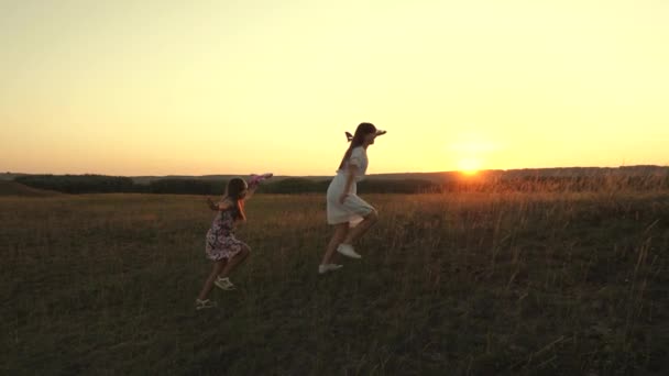 Sueños de volar. Concepto de infancia feliz. Dos chicas juegan con un avión de juguete al atardecer. Niños en el fondo del sol con un avión en la mano. Silueta de niños jugando en el avión — Vídeos de Stock