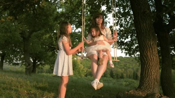 Maman marche avec les enfants et se balance sur une balançoire dans le parc. Le concept d'une famille heureuse. rêve de voler. Le concept d'une famille heureuse et de l'enfance. mère et filles jouant dans le parc . — Video