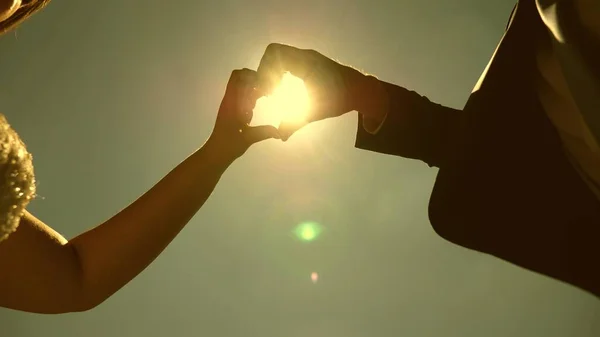 Sol en la mano. Silueta de una pareja amorosa haciendo un símbolo del corazón con sus manos frente al sol en el horizonte. Trabajo en equipo de pareja amorosa. Día de la boda celebración — Foto de Stock