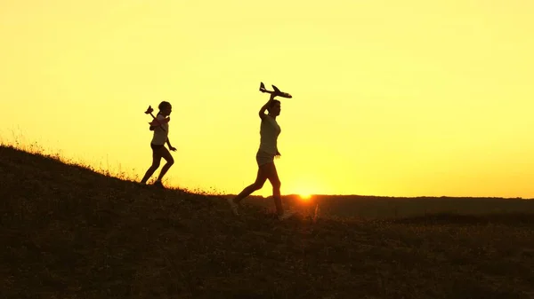 Sueños de volar. Concepto de infancia feliz. Dos chicas juegan con un avión de juguete al atardecer. Niños en el fondo del sol con un avión en la mano. Silueta de niños jugando en el avión — Foto de Stock