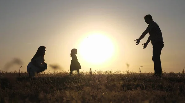 Föräldrar leker med sin lilla dotter. Glad baby går från pappa till mamma. Glad barndom. Föräldrar får lära sig att gå med ett litet barn. liten flicka gör sina första steg i solen, slow motion. — Stockfoto