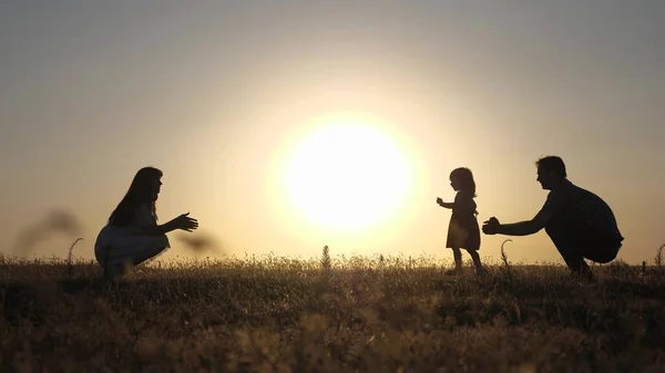 Padres juegan con su hijita. bebé feliz va de papá a mamá. concepto de infancia feliz. a los padres se les enseña a caminar a un niño pequeño. niña hace sus primeros pasos en el sol, cámara lenta . — Foto de Stock