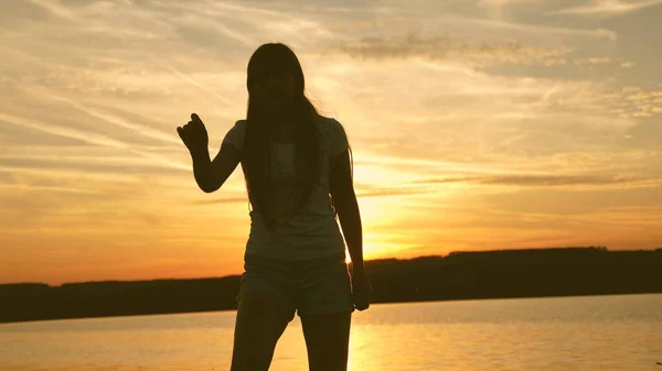 Μια νεαρή γυναίκα χορεύει σε ένα πάρτι στο ηλιοβασίλεμα. Ελεύθερη και χαρούμενη γυναίκα. Ευτυχισμένο κορίτσι με μακριά μαλλιά χορεύει το ηλιοβασίλεμα στην παραλία και γελάει. Αργή κίνηση. — Φωτογραφία Αρχείου