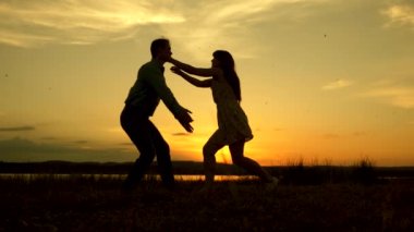 Mutlu adam ve kız yaz parkında akşam vals. Sevgi dolu erkek ve kadın gölün arka planda güneşin parlak ışınları dans. Genç çift sahilde gün batımında dans.