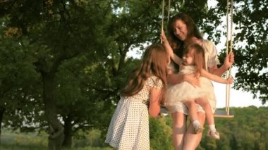 Anne kızlarını güneşin altında salıncakta sallıyor, çocuklarla oynuyor. çocukluk ve aile kavramı. Anne ve bebek halatla ormanda meşe dalında salıncakta sallanıyor. Kız güler, sevinir..