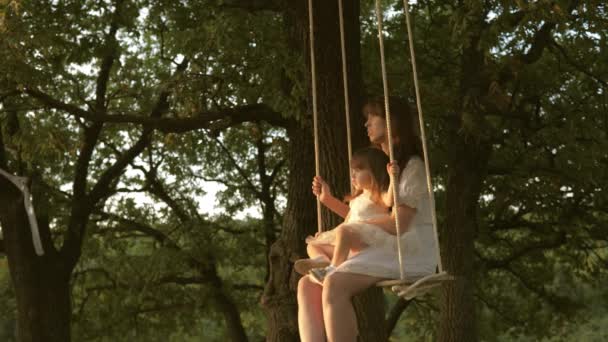 Begreppet lycklig familj och barndom. Mamma och dotter leker i parken på sommaren, våren. Lycklig mamma skakar söt bebis på en gunga i en park på ett träd. begreppet lycklig familj. dröm om att flyga. — Stockvideo