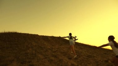 Çocuklar gün batımında ellerinde bir uçakla dağa koşuyorlar. Uçma hayalleri. Uçakta oynayan çocukların silueti. Mutlu çocukluk kavramı. Kızlar gün batımında oyuncak uçakla oynarlar..