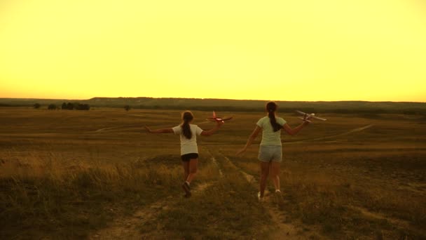 Silhouet van kinderen die in het vliegtuig spelen. Kinderen rennen van de berg met een vliegtuig in de hand tegen de achtergrond van de zon. Dromen van vliegen. Gelukkige kindertijd concept. meisjes spelen met een speelgoedvliegtuig bij zonsondergang. — Stockvideo