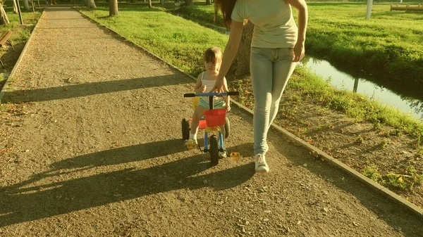 Malé dítě se naučí jezdit na kole po boku své matky. Máma učí dceru jezdit na kole v parku. Matka si hraje se svou dcerou. Koncept šťastného dětství. — Stock fotografie