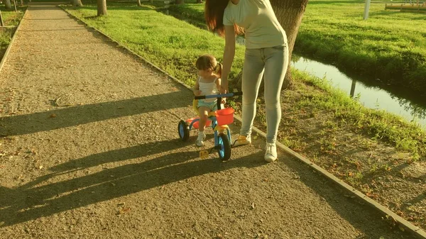 Ett litet barn lär sig cykla med sin mamma. Mamma lär dottern cykla i parken. Mor leker med sin lilla dotter. Begreppet lycklig barndom. — Stockfoto