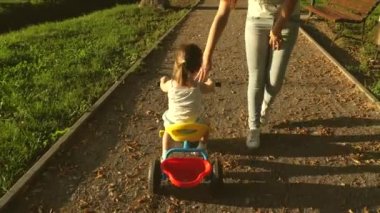 Annesi kızına parkta bisiklet sürmeyi öğretiyor. Küçük bir çocuk bisiklet sürmeyi öğrenir. Anne küçük kızıyla oynuyor. Mutlu çocukluk kavramı. Hafta sonu aile tatili..