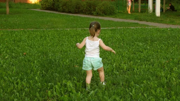 Niño feliz corre en un prado en verano sobre una hierba verde. niña alegre corre a través del campo. concepto de felicidad. niño juega en el césped en el verano. En cámara lenta. bebé juega en el parque en primavera. — Foto de Stock