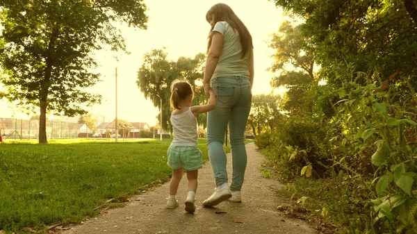 Kleine Tochter und Mutter gehen Hand in Hand. Baby hält Mamas Hand. Mutter und Baby ruhen sich im Park aus. Das Konzept einer glücklichen Kindheit. Eine glückliche Familie mit Kind spaziert abends aus der Stadt. — Stockfoto