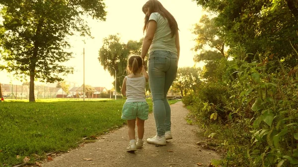 Little daughter and mom walk path holding hands. baby holds moms hand. Mother and baby rest in park. The concept of a happy childhood. A happy family with a child walks in evening out of town. — Stock Photo, Image