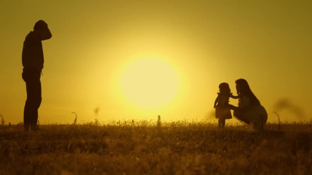 Parents play with their little daughter in the park.happy child goes from dad to mom across the field. parents are taught to walk a small child, little girl makes her first steps in sun, slow motion. — Stock Video