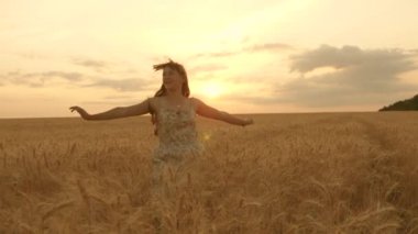 Mutlu genç kız tarlada ağır çekimde koşuyor, buğday başaklarına eliyle dokunuyor. Güzel, özgür bir kadın günbatımı arka planındaki buğday tarlasında güneşin altında doğanın tadını çıkarıyor. Kız seyahat eder.