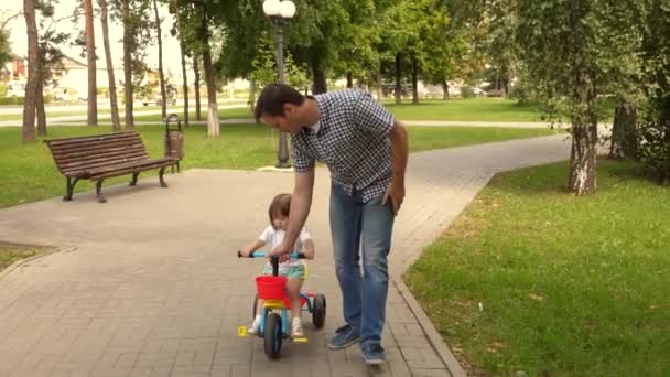 Papa spielt mit seinem Kind im Freien. Kind lernt Fahrradfahren. Konzept einer glücklichen Familie und Kindheit. Eltern und kleine Tochter spazieren im Park. Glücklicher Vater lehrt kleine Tochter Fahrradfahren. — Stockvideo